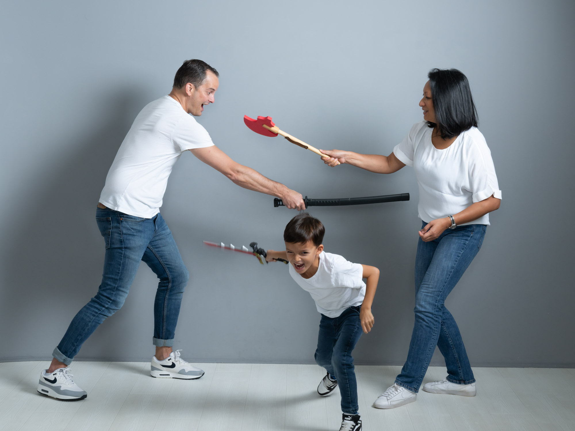 Portrait de famille joyeuse au Studio Ah! – Séance photo ludique avec des fausses épées, capturant des moments de complicité et de fun.